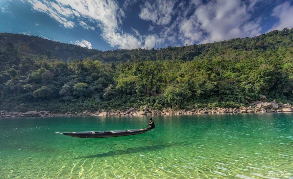 Crystal clear river water and a traditional boat surrounded by lush green hills in Cherrapunji, Meghalaya.