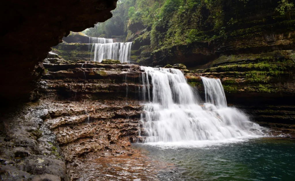 Beautiful multi-layered waterfall in Cherrapunji surrounded by rocky caves, lush greenery, and peaceful natural landscapes.