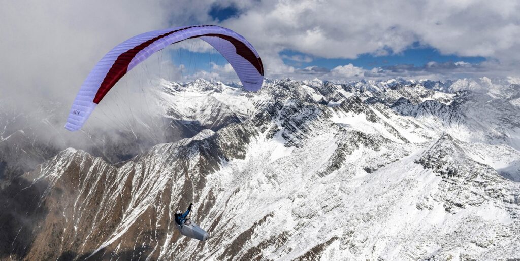 Paragliding adventure over snow-covered Himalayan mountains with a colorful parachute soaring through the cloudy sky.